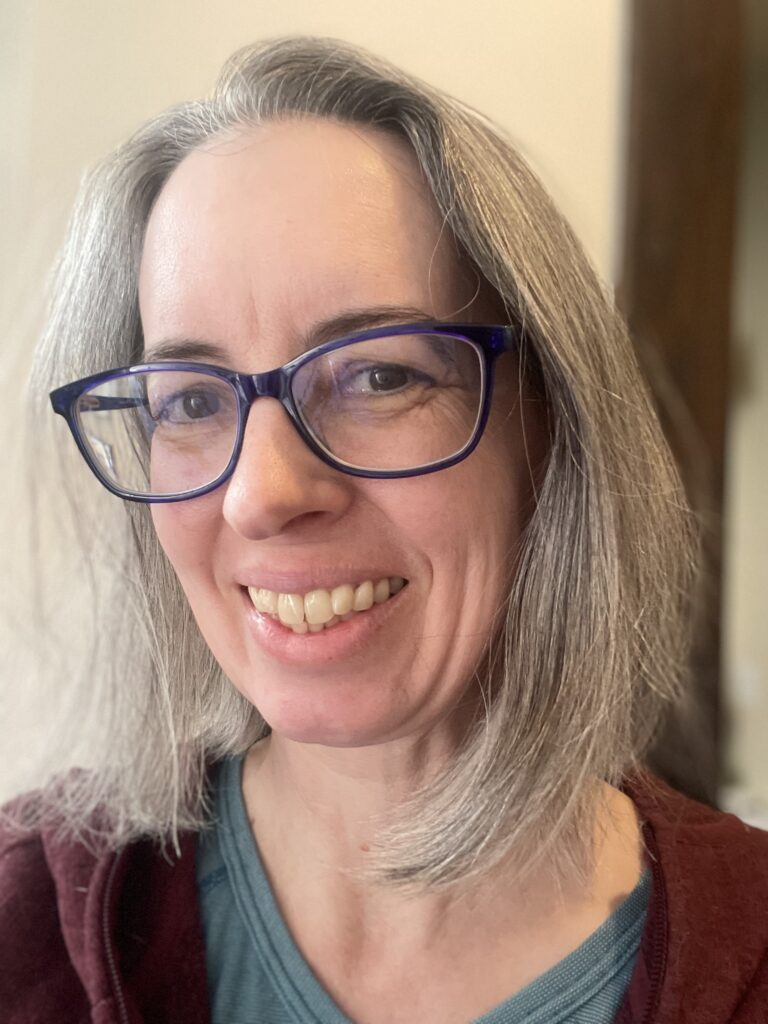 A white woman with grey hair and glasses smiles warmly.